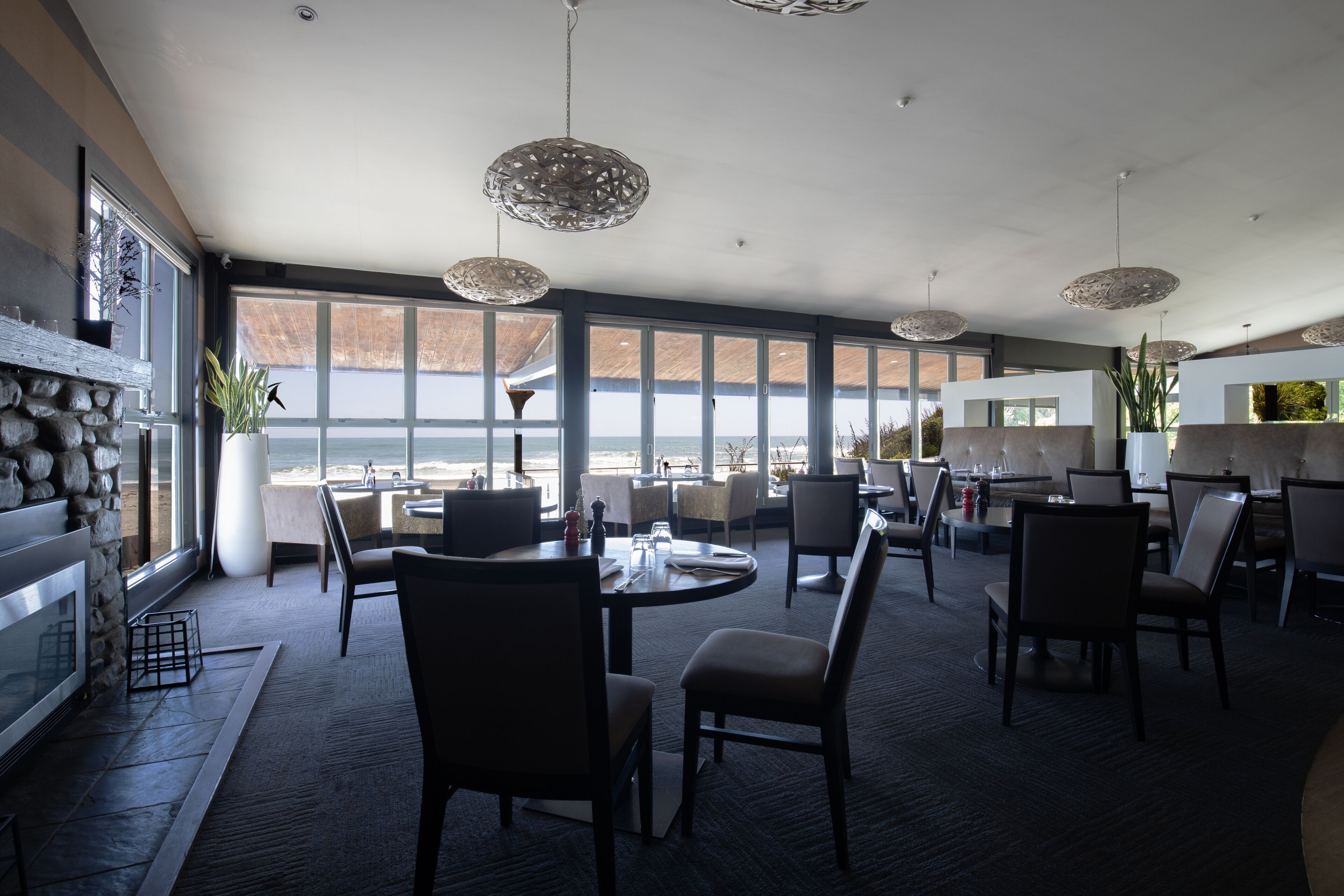 A spacious dining area with large windows, modern pendant lighting, and a stone fireplace.
