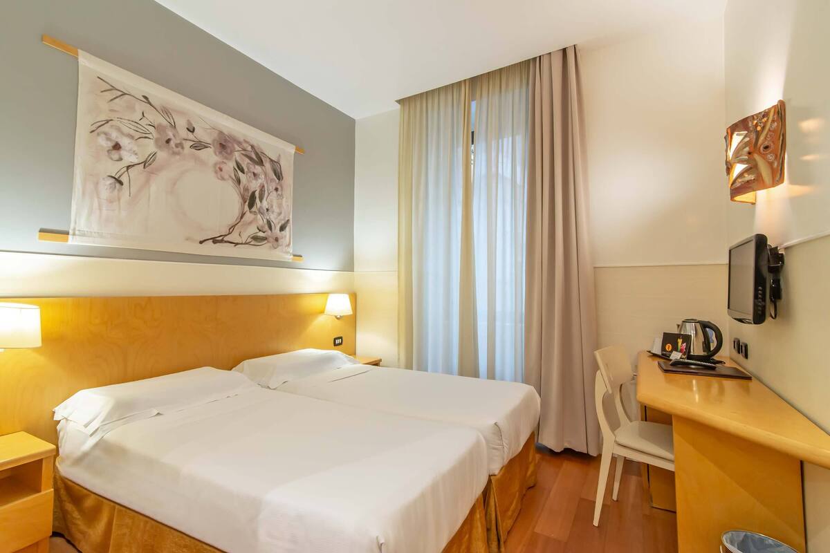 Una camera d'albergo con due letti, una scrivania con una sedia, una televisione e un quadro appeso al muro.