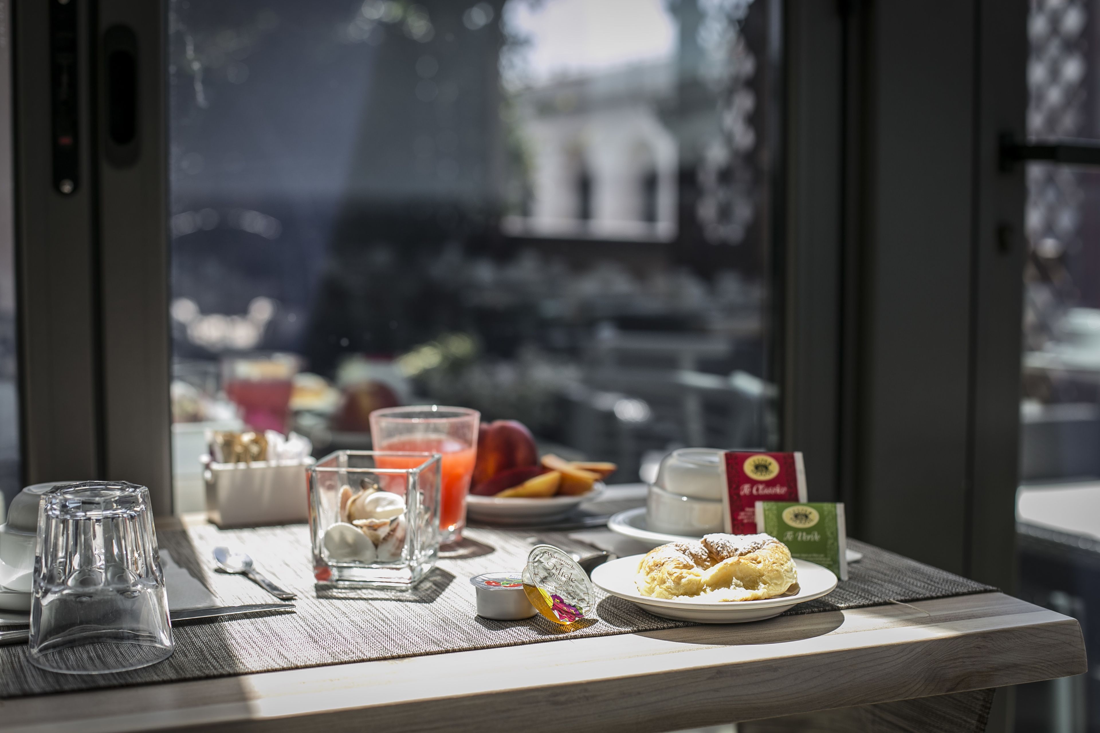 Une table de petit-déjeuner avec un verre de jus d’orange, une assiette de viennoiseries et une brique de lait.