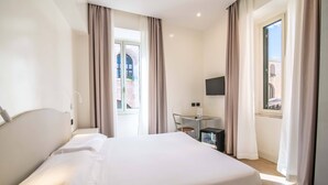 Una habitación de hotel con cama, escritorio, televisión y ventana con cortinas.