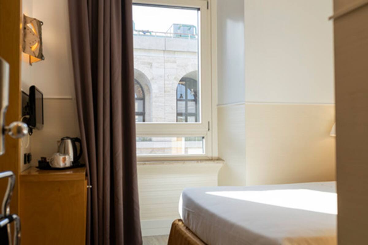 Una camera d'hotel con un letto, una scrivania in legno con un bollitore e una finestra con tende.