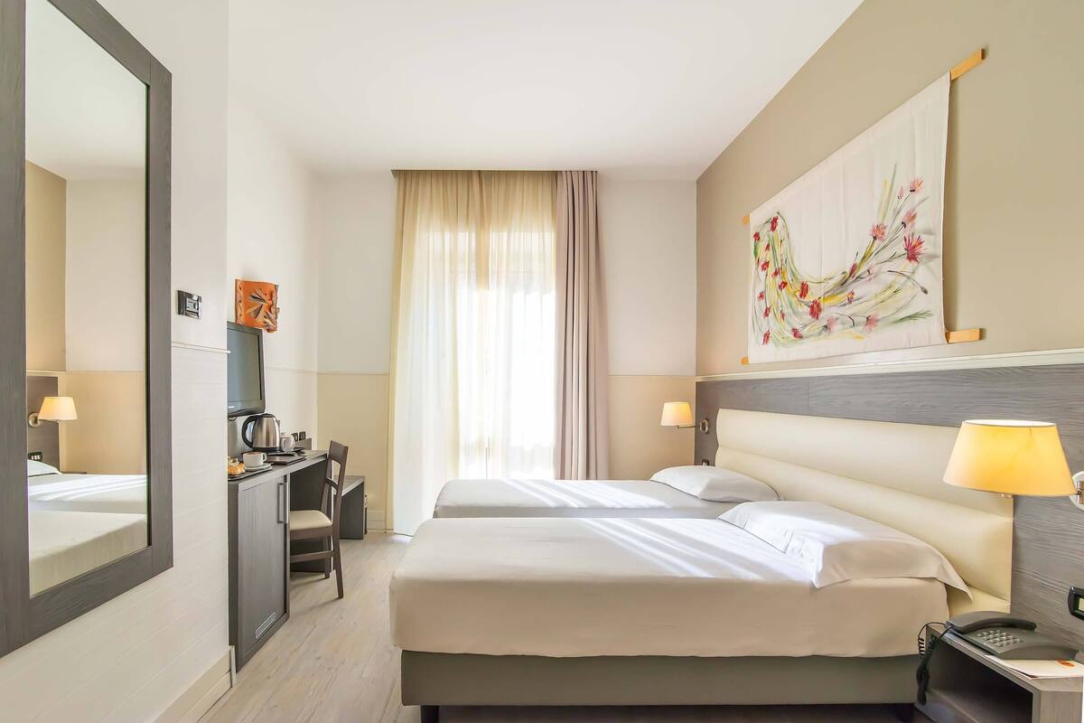 Una camera d'albergo con un letto, una scrivania, una sedia e uno specchio grande.
