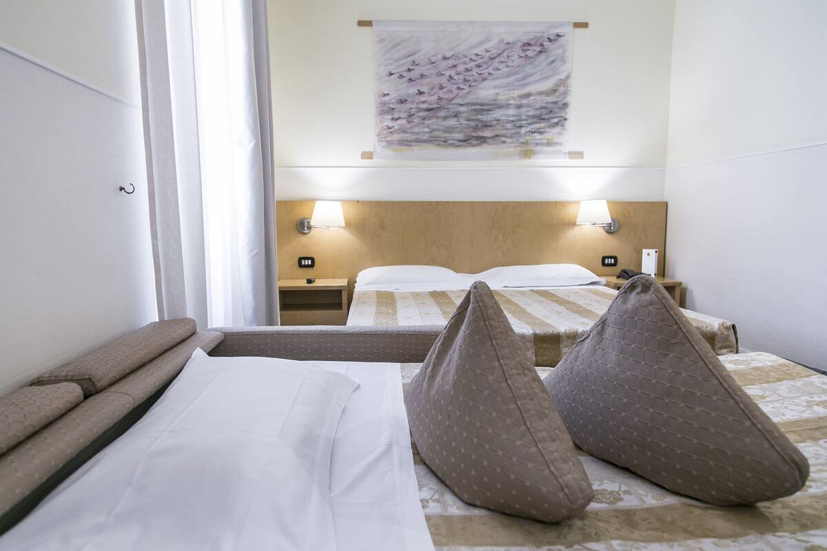 Camera d'albergo con due letti, ognuno con cuscini e testiera. Sono presenti comodini con lampade e un'opera d'arte appesa sopra i letti.