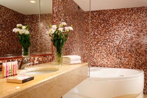A bathroom with a mosaic tile wall, a sink, a mirror, and a bathtub.