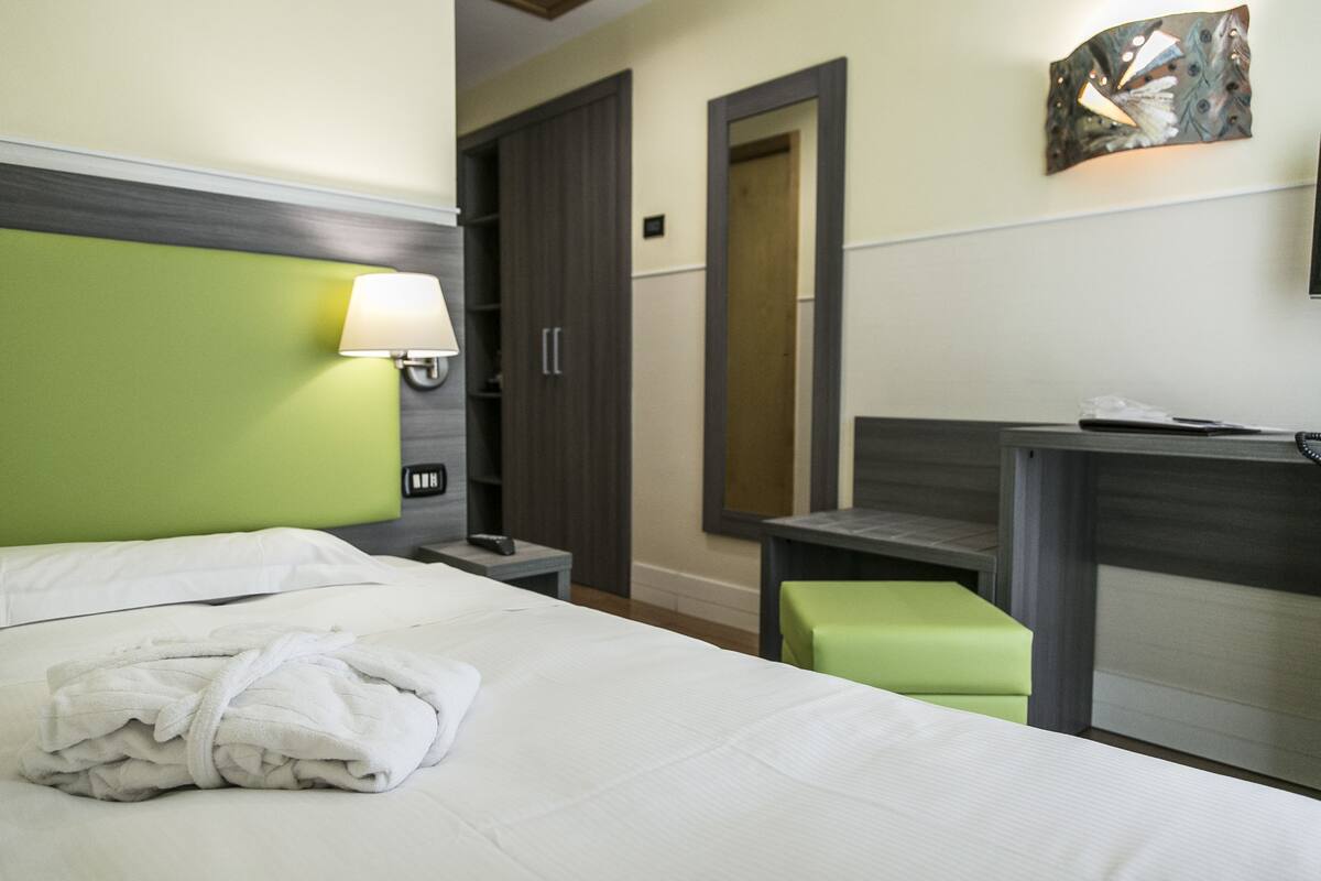 Una camera d'albergo con un letto, una scrivania, una sedia, una lampada e un armadio.