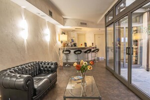 A modern lobby with a leather sofa, a glass coffee table with a vase of flowers, and a bar area with stools.
