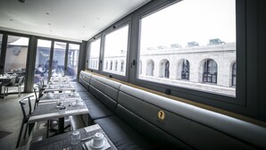 Un restaurante con amplios ventanales, una zona de asientos con un largo banco y mesas dispuestas para comer.
