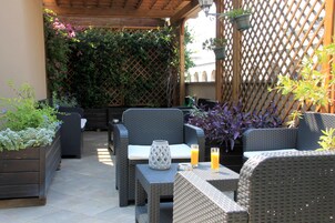 A covered patio area with wicker furniture, a table with drinks, and potted plants.