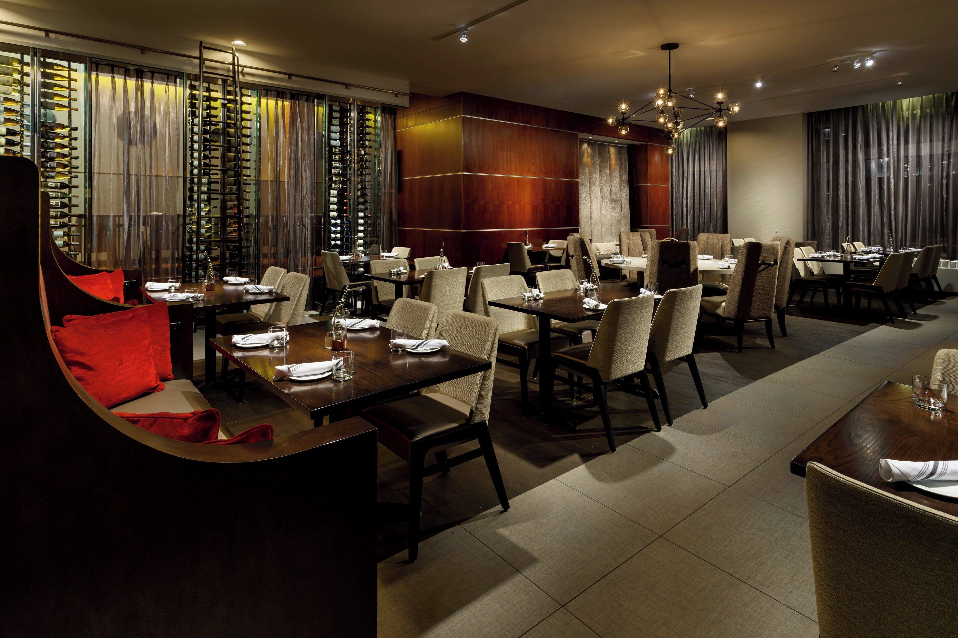 Un restaurant moderne doté de plusieurs tables et chaises, d’un meuble à vin et d’un coin salon confortable agrémenté d’un coussin rouge.