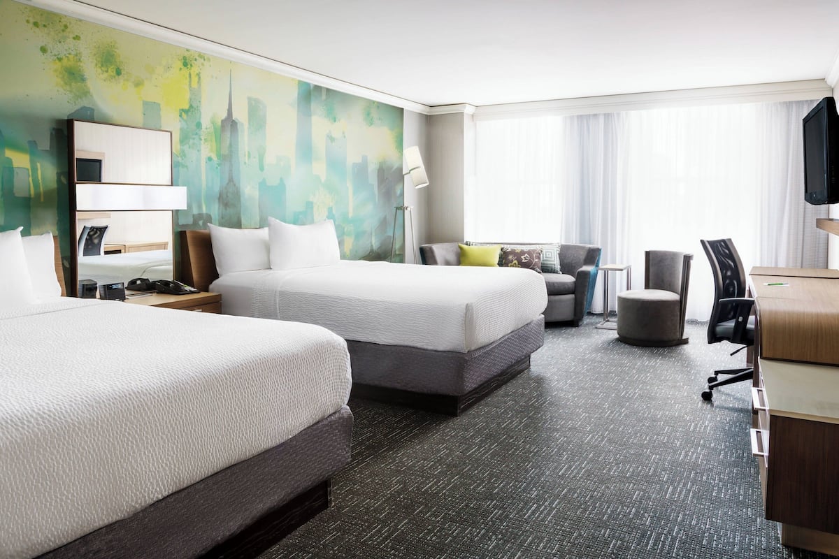 A hotel room with two beds, a desk, a chair, a sofa, and a television.