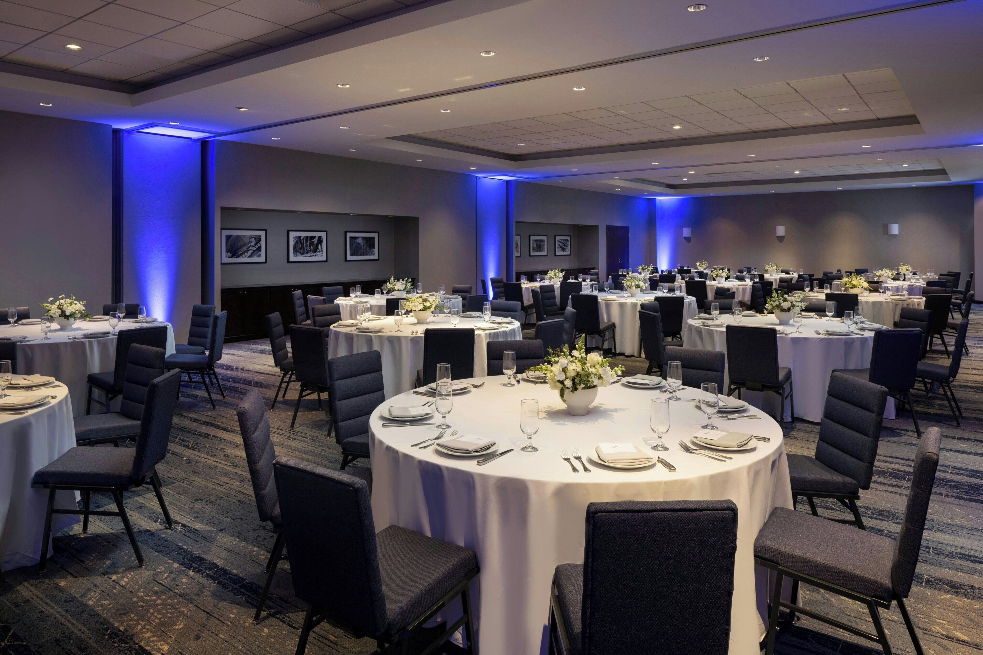 Un salón de conferencias con varias mesas redondas, cada una con sillas, platos y cubiertos.
