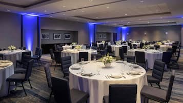 Un salón de conferencias con varias mesas redondas, cada una con sillas, platos y cubiertos.