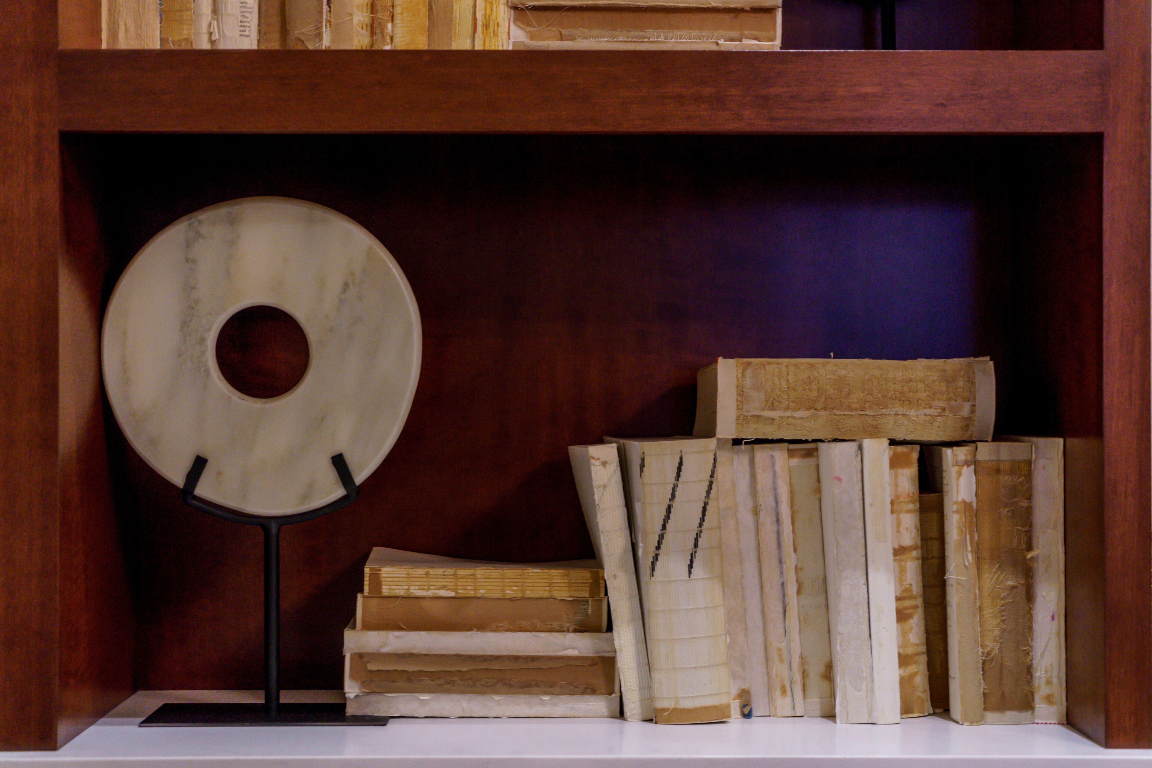 A wooden bookshelf with a circular object on a stand, surrounded by old books.