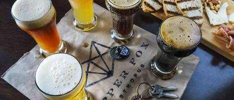 A table with various glasses of beer, a platter of cheese and meats, and a coaster with a logo.