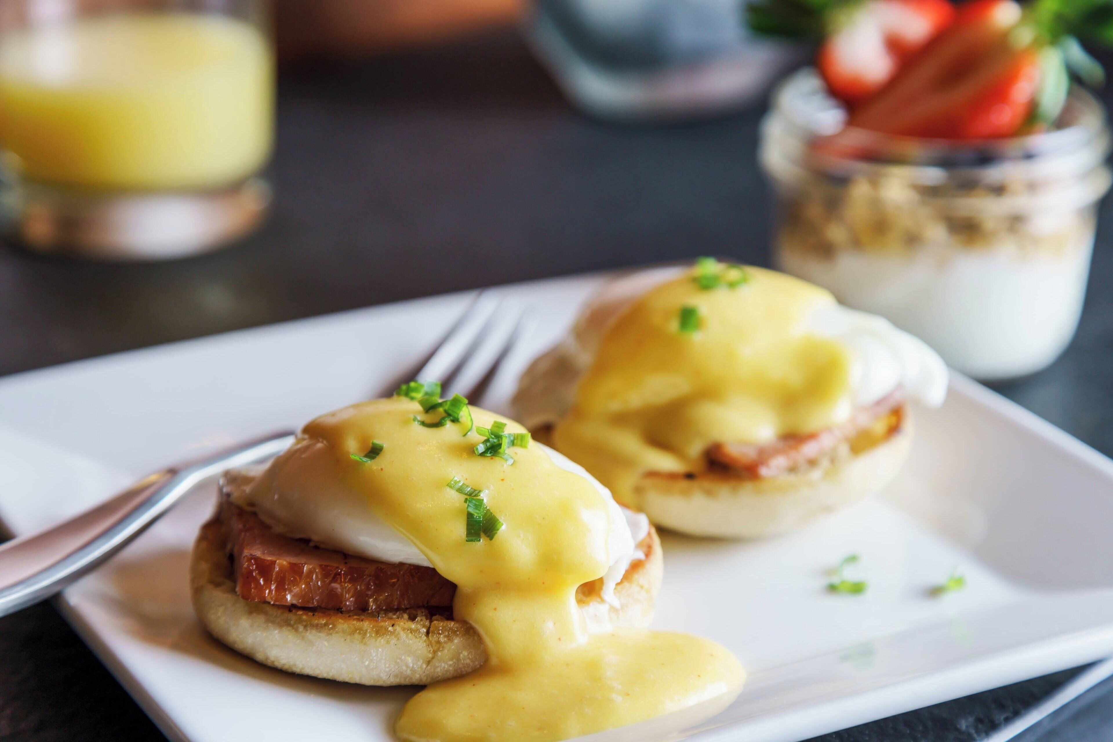 A plate with two eggs benedict sandwiches garnished with chives.