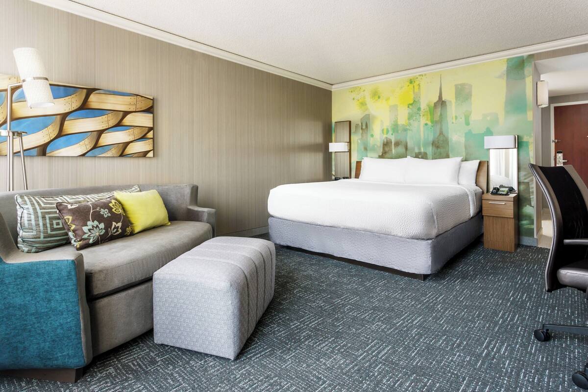 A hotel room with a bed, a sofa, an ottoman, a desk, and a chair.