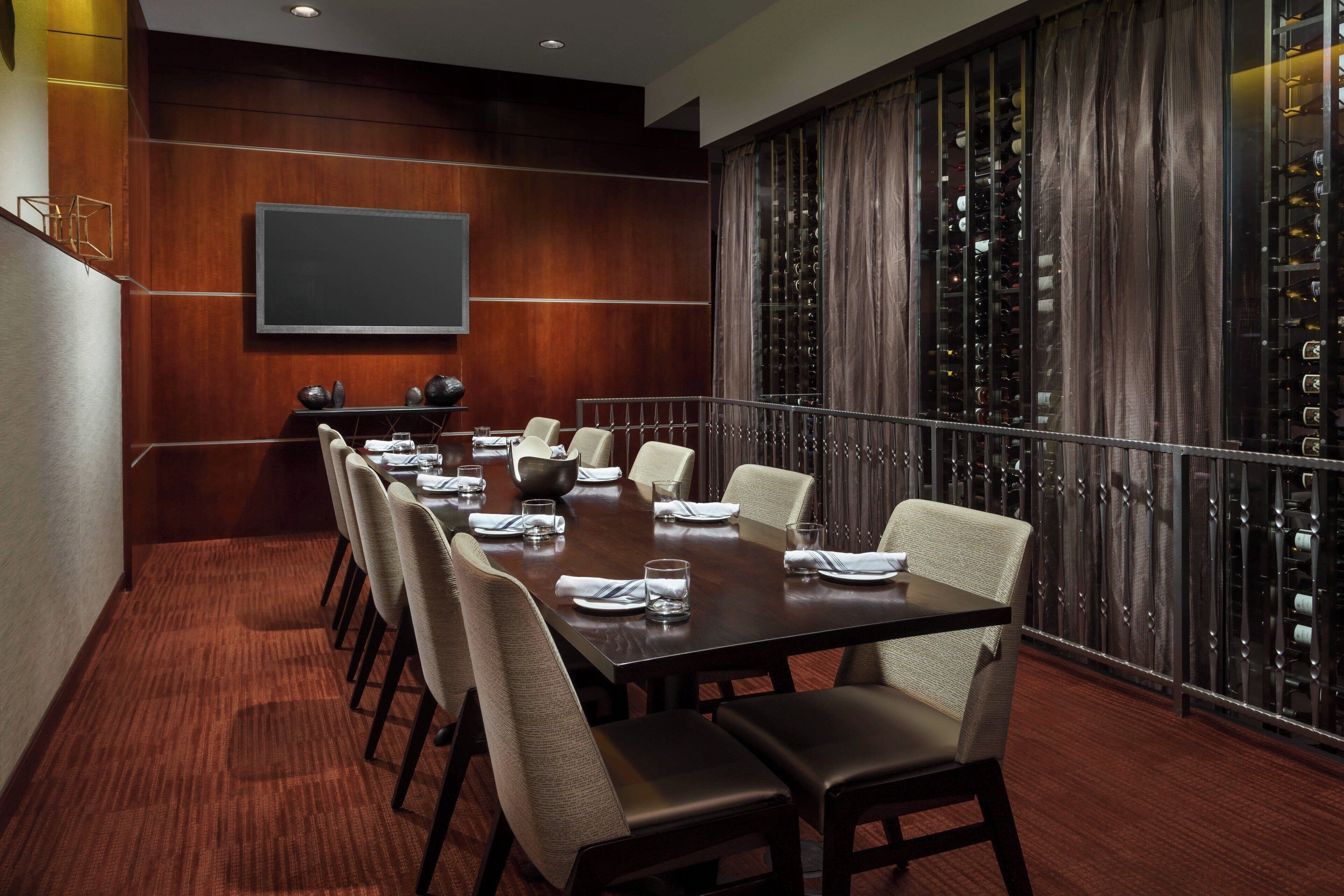 A conference room with a long table, chairs, a screen, and wine racks.