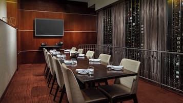 A conference room with a long table, chairs, a screen, and wine racks.