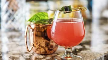 A copper mug and a glass with a red drink, garnished with a leaf, on a marble surface.
