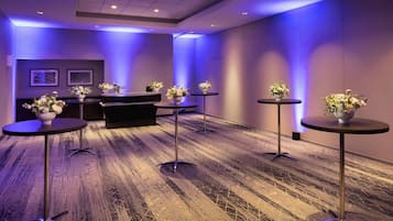 Un salón de conferencias con una mesa larga, cuatro mesas redondas con jarrones de flores y suelo alfombrado.