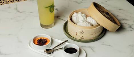 A table with a drink, a bamboo container with a lid, a small bowl with sauce, and a spoon on a tray.