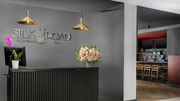 A reception desk with a modern design, a sign reading "SILK ROAD ASIAN TAPAS EAT," and a flower arrangement. - Courtyard by Marriott Houston Rice University (Houston)