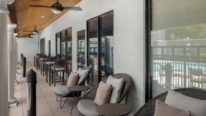 A covered outdoor seating area with wicker furniture, ceiling fans, and large windows overlooking a pool. - Courtyard by Marriott Houston Rice University (Houston)