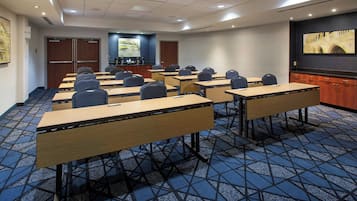 A conference room with multiple tables and chairs, a projector screen, and a coffee station.