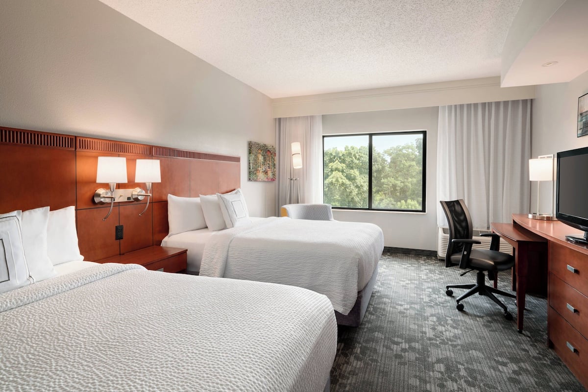 Une chambre d’hôtel avec deux lits, un bureau, une chaise et un téléviseur.