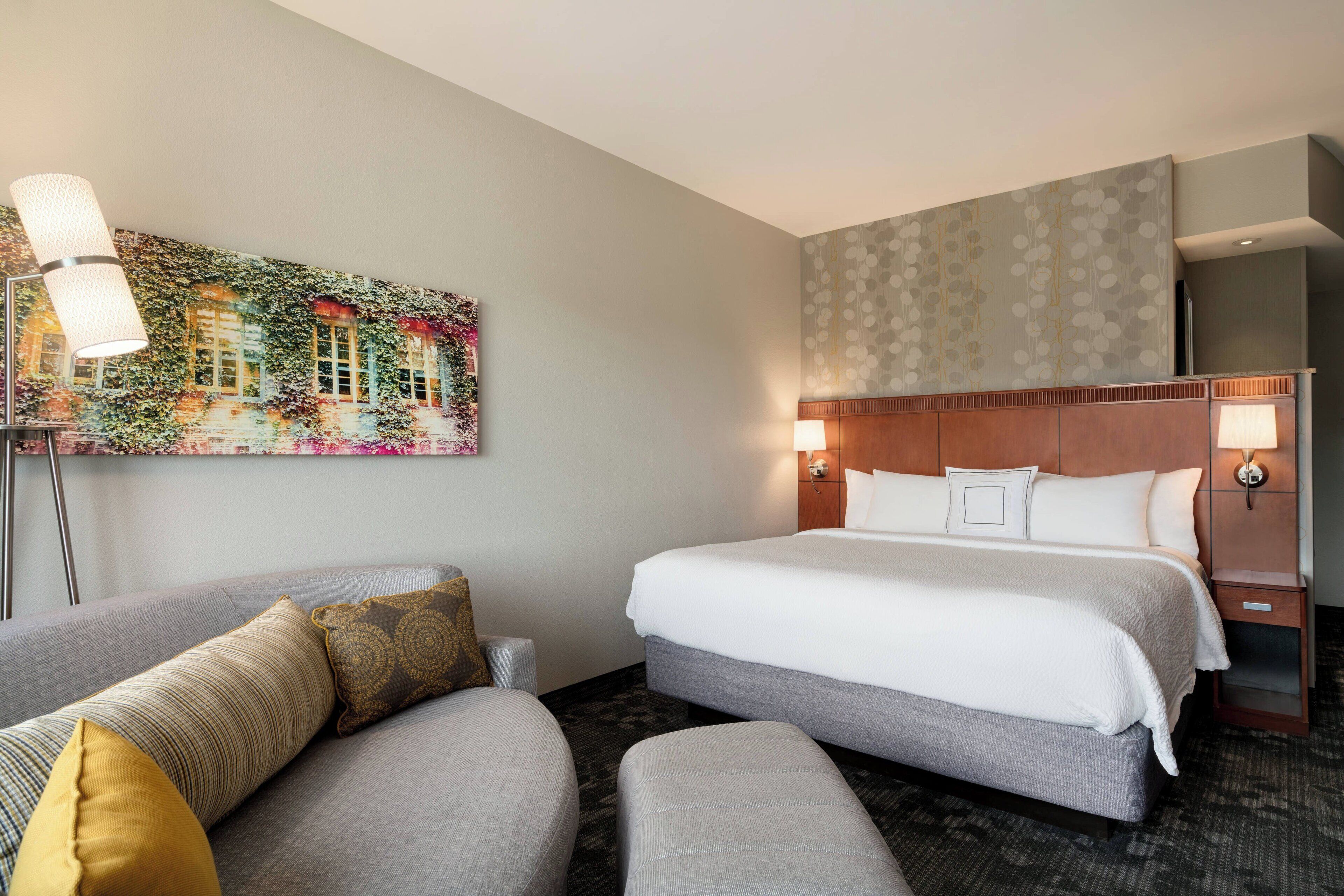 Une chambre d’hôtel avec un grand lit, deux tables de chevet avec des lampes, un canapé avec des coussins et une fresque murale.