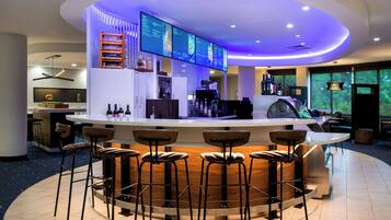 Zona de bar moderna con mostrador curvo, varios taburetes y una pantalla de menú.