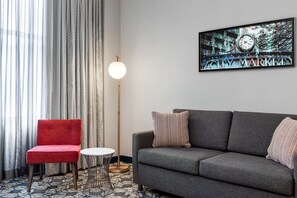 A modern living room with a red chair, grey sofa, and a round table. A floor lamp and a painting of a clock are also visible. - Hilton Garden Inn Indianapolis Downtown (Indianapolis)