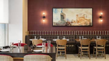 Interior de restaurante con pintura de paisaje urbano, cabinas acolchadas y mesas redondas.