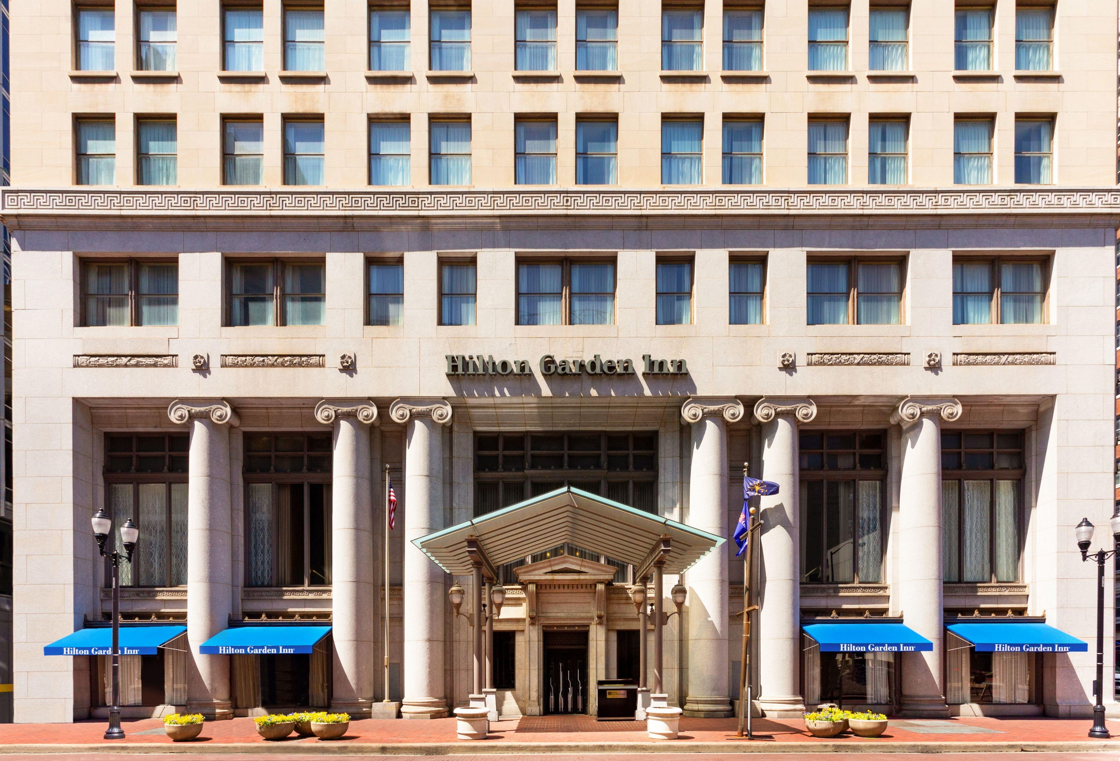 Un edificio de estilo arquitectónico clásico, con una entrada central con frontón sostenido por columnas, y el nombre 'Hilton Garden Inn' exhibido en la parte superior.