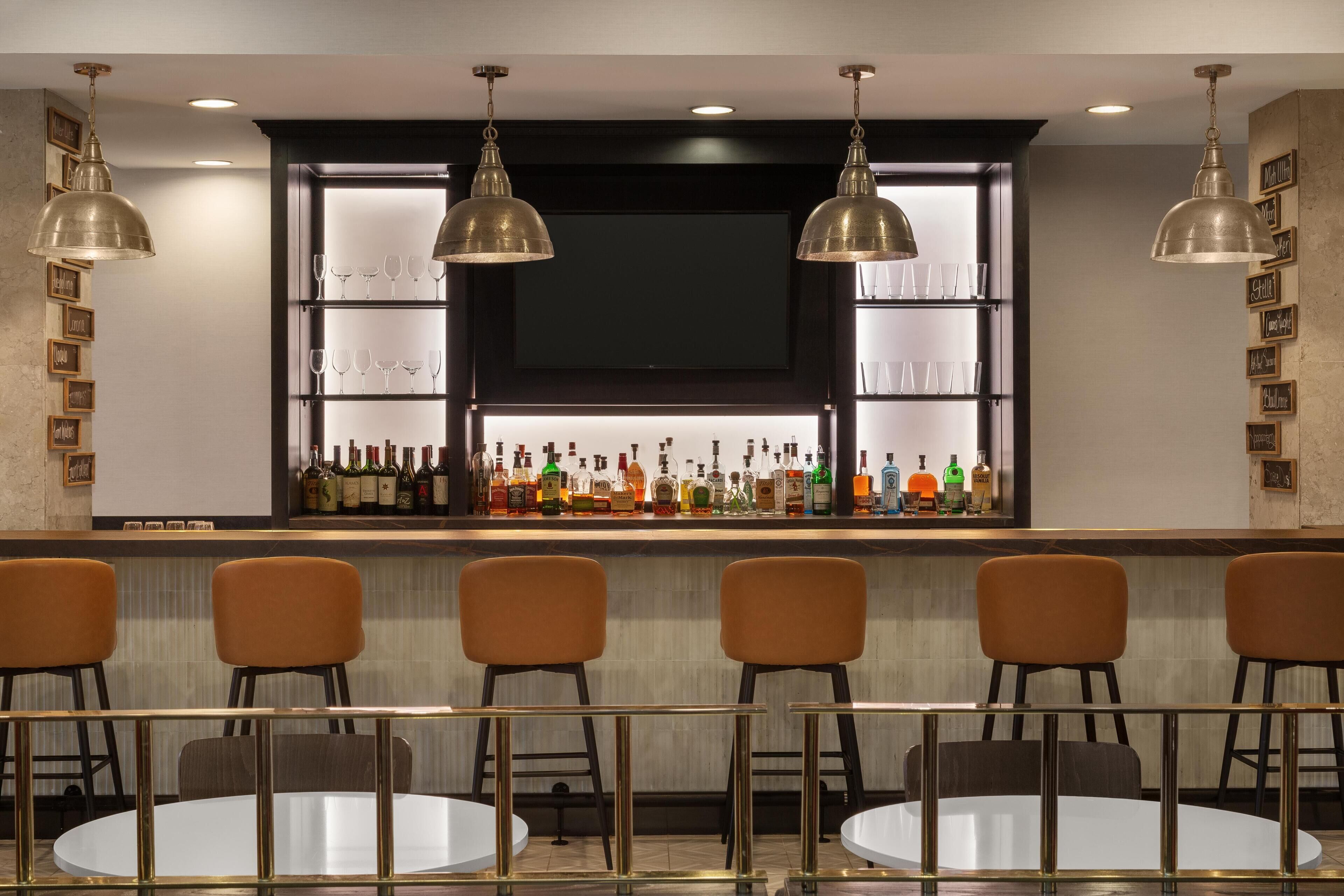 A bar area with multiple chairs and tables, a shelf with bottles, and pendant lighting.
