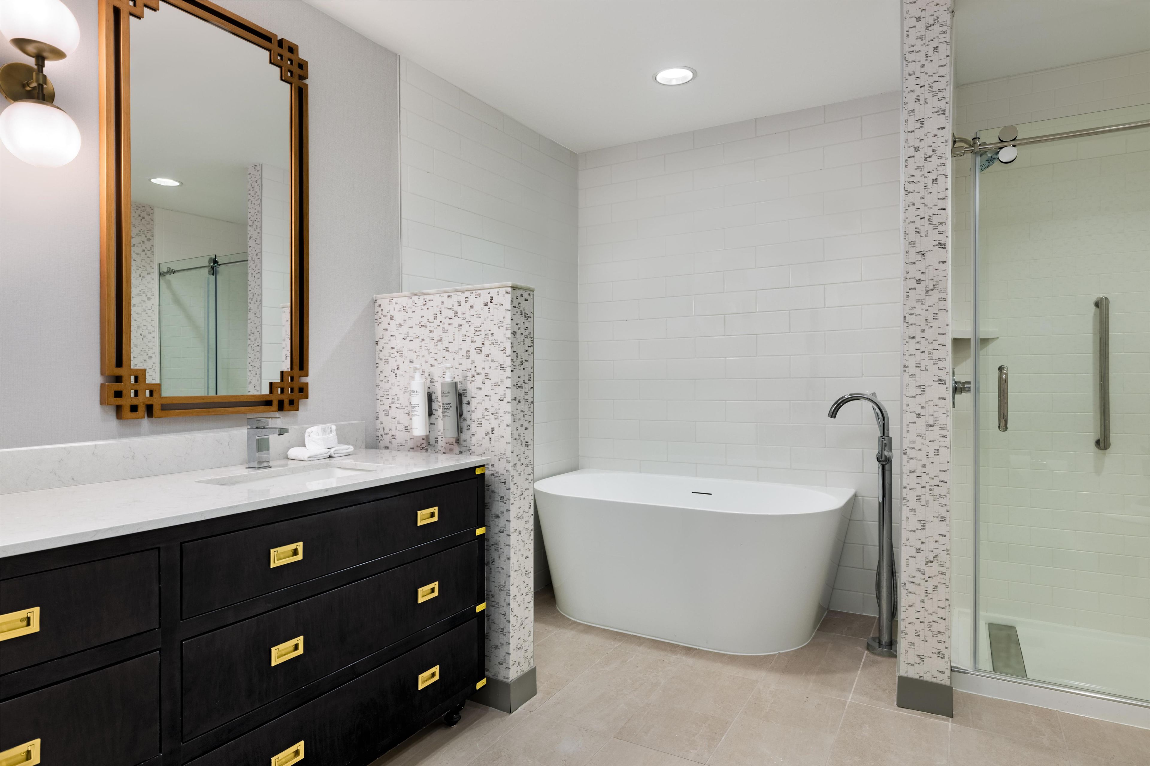 A modern bathroom with a freestanding bathtub, a large mirror, and a vanity with black cabinets.