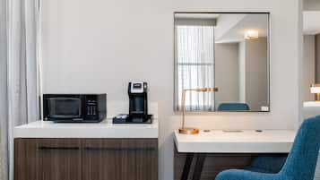 Habitación de hotel con kitchenette, microondas, cafetera, escritorio, silla y espejo.
