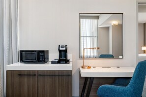 A hotel room with a kitchenette, a microwave, a coffee maker, a desk, a chair, and a mirror. - Hilton Garden Inn Indianapolis Downtown (Indianapolis)