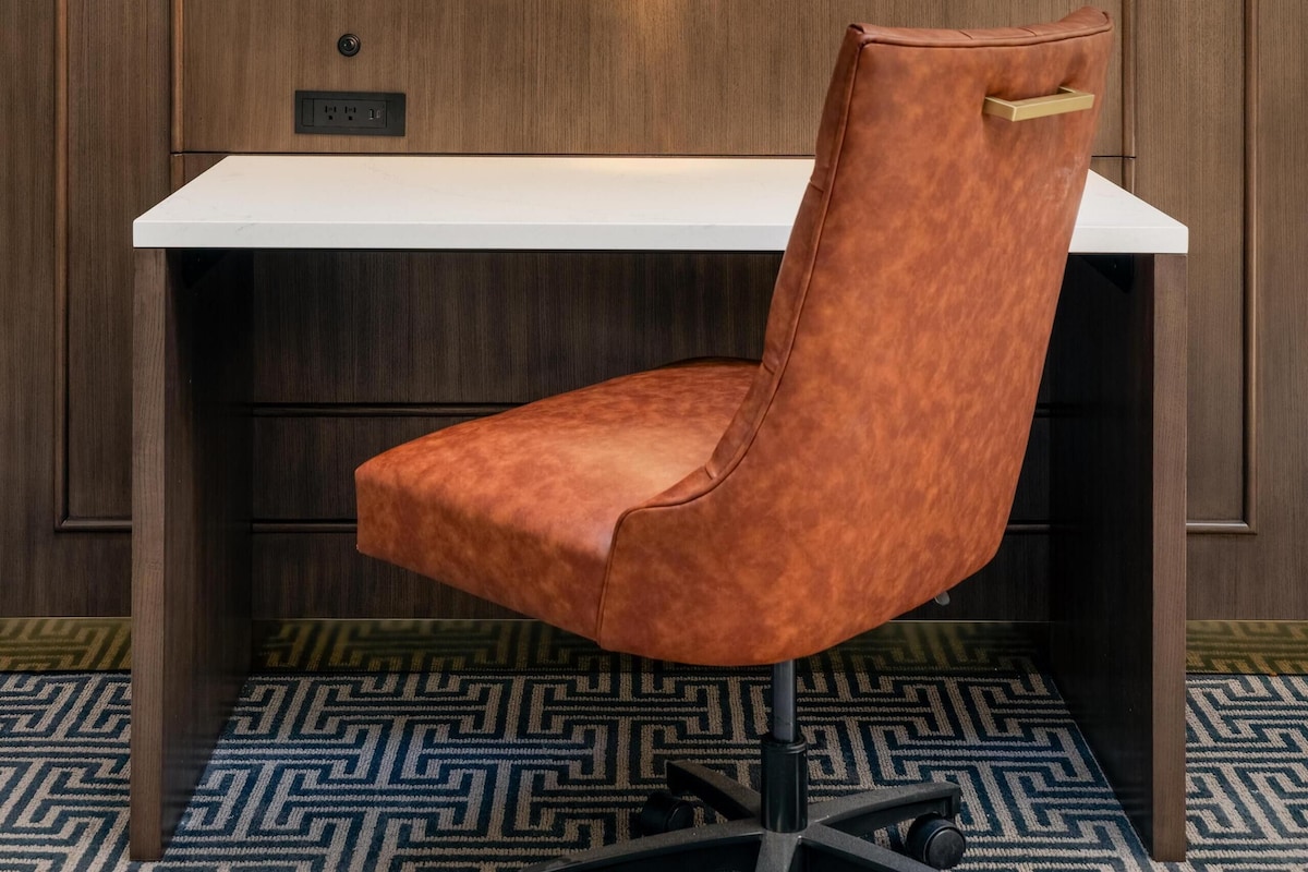 A modern desk with a leather chair, a wall-mounted light fixture, and a patterned floor.