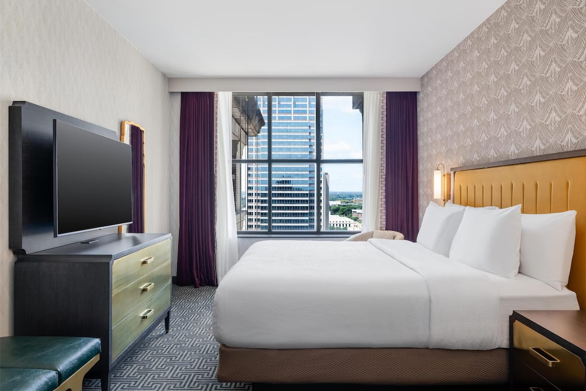 Ein Hotelzimmer mit einem großen Bett, einem Flachbildfernseher, einem Schreibtisch und einem Fenster mit Blick auf die Stadt.