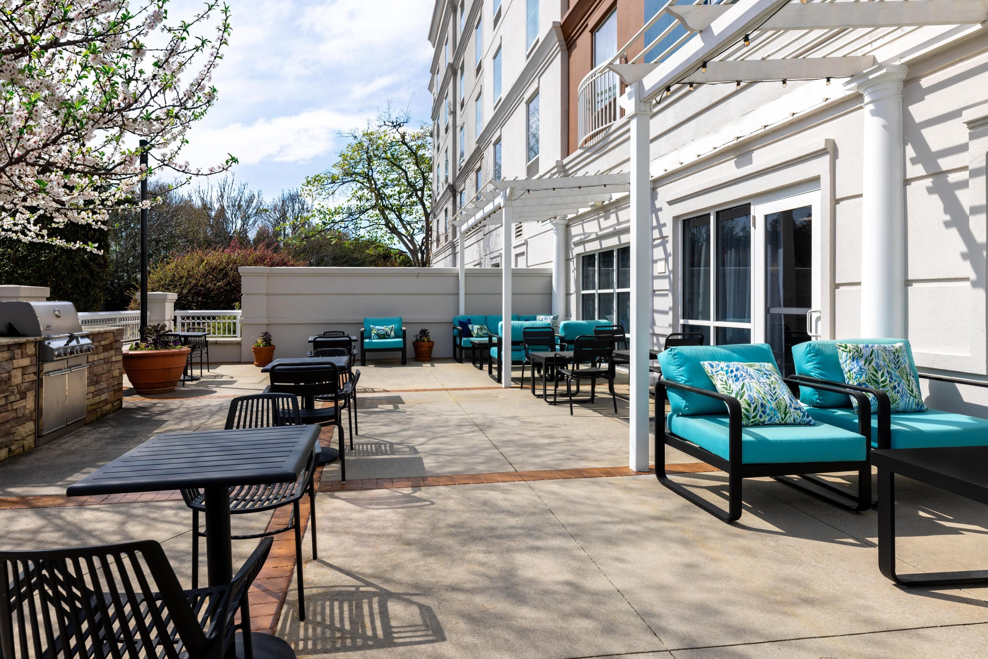 A covered outdoor patio with seating, a grill, and potted plants.