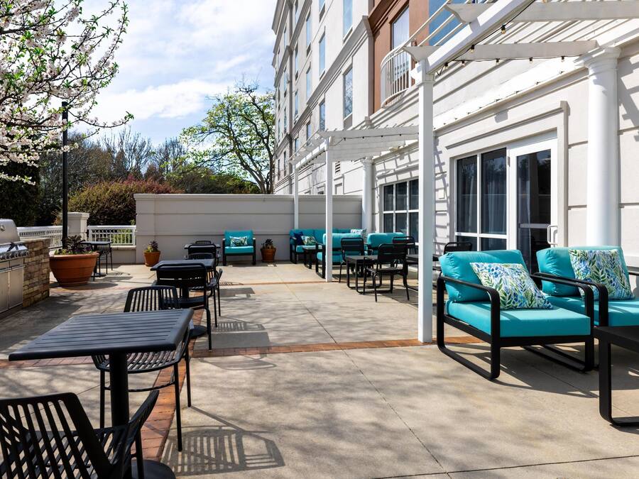 A covered outdoor patio with seating, a grill, and potted plants.