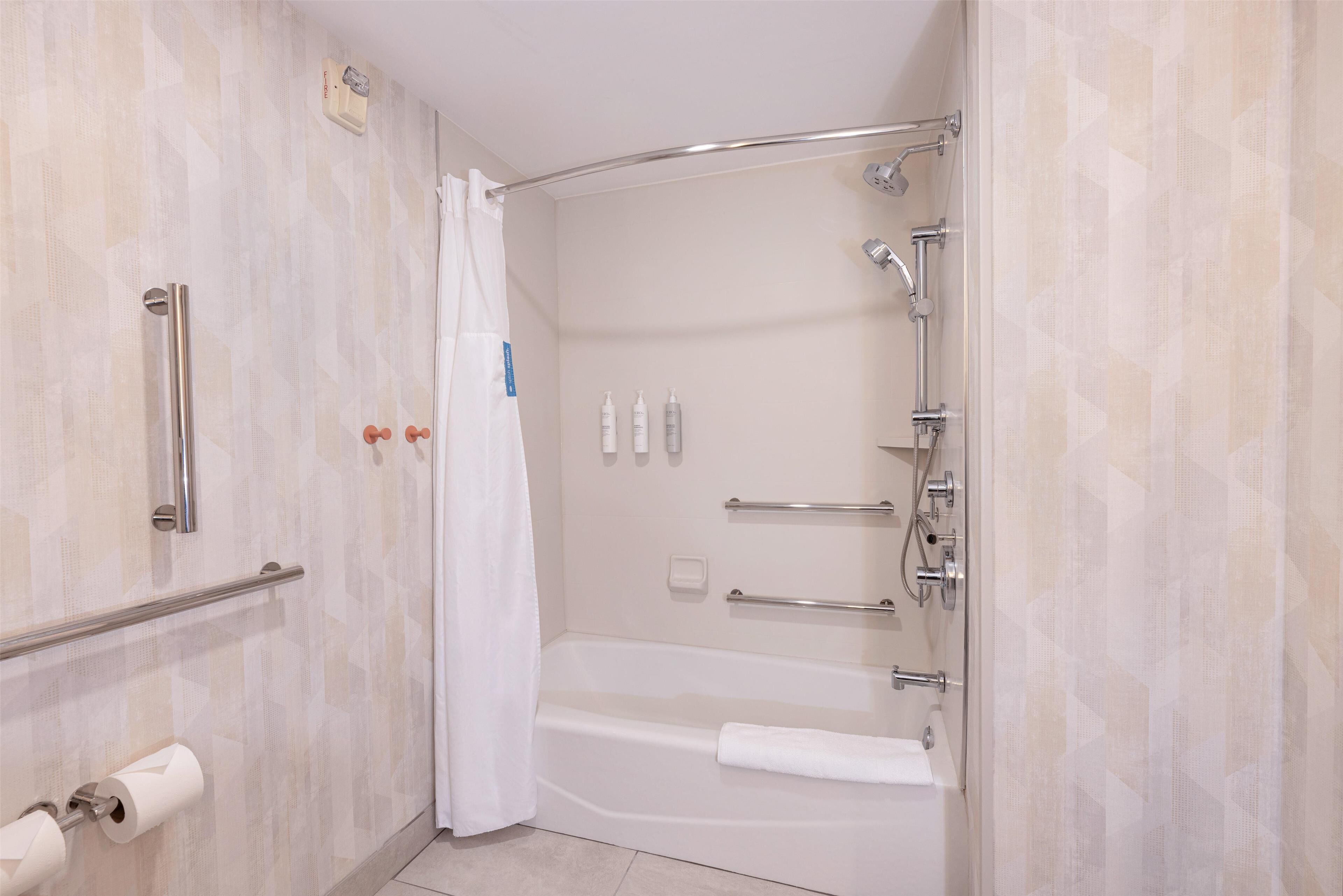 Um banheiro moderno com chuveiro de acesso facilitado, barras de apoio, porta-toalhas e suporte para papel higiênico.
