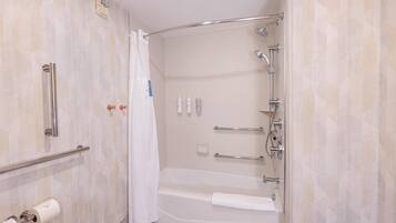 Um banheiro moderno com chuveiro de acesso facilitado, barras de apoio, porta-toalhas e suporte para papel higiênico.