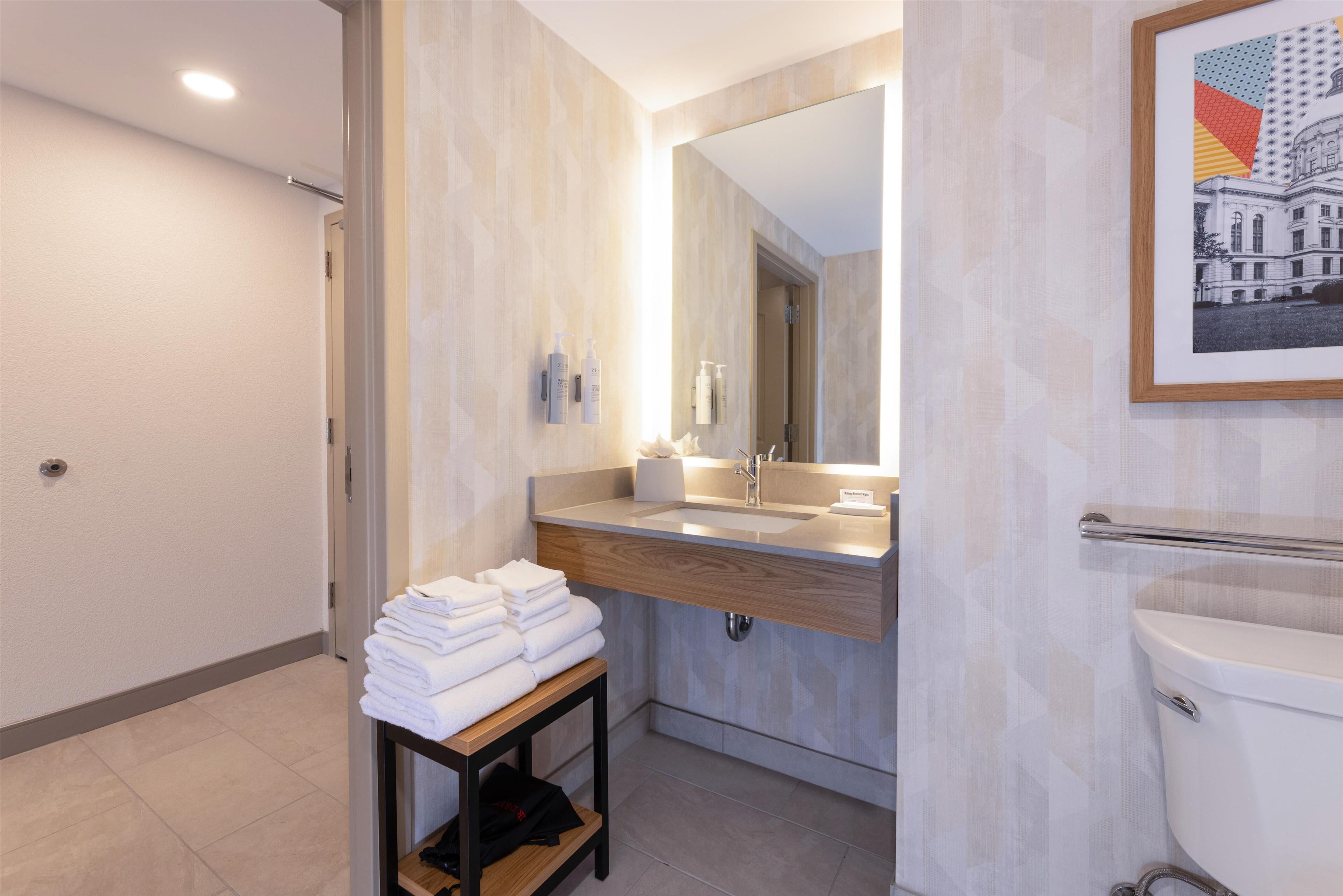 A modern bathroom with a wooden vanity, a large mirror, and a framed picture on the wall.