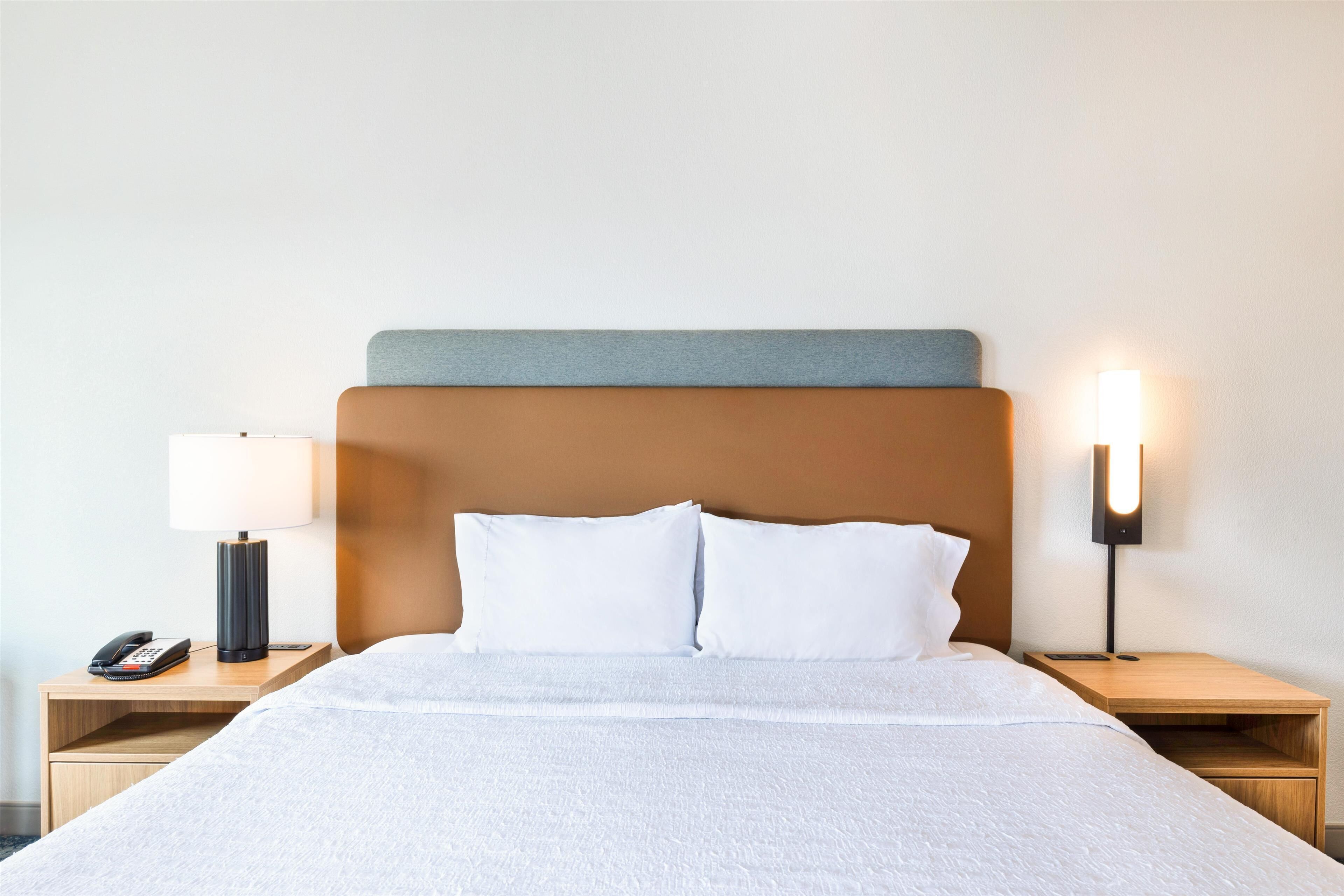 A neatly made bed with white linens, a wooden headboard, and two bedside tables with lamps and a phone.