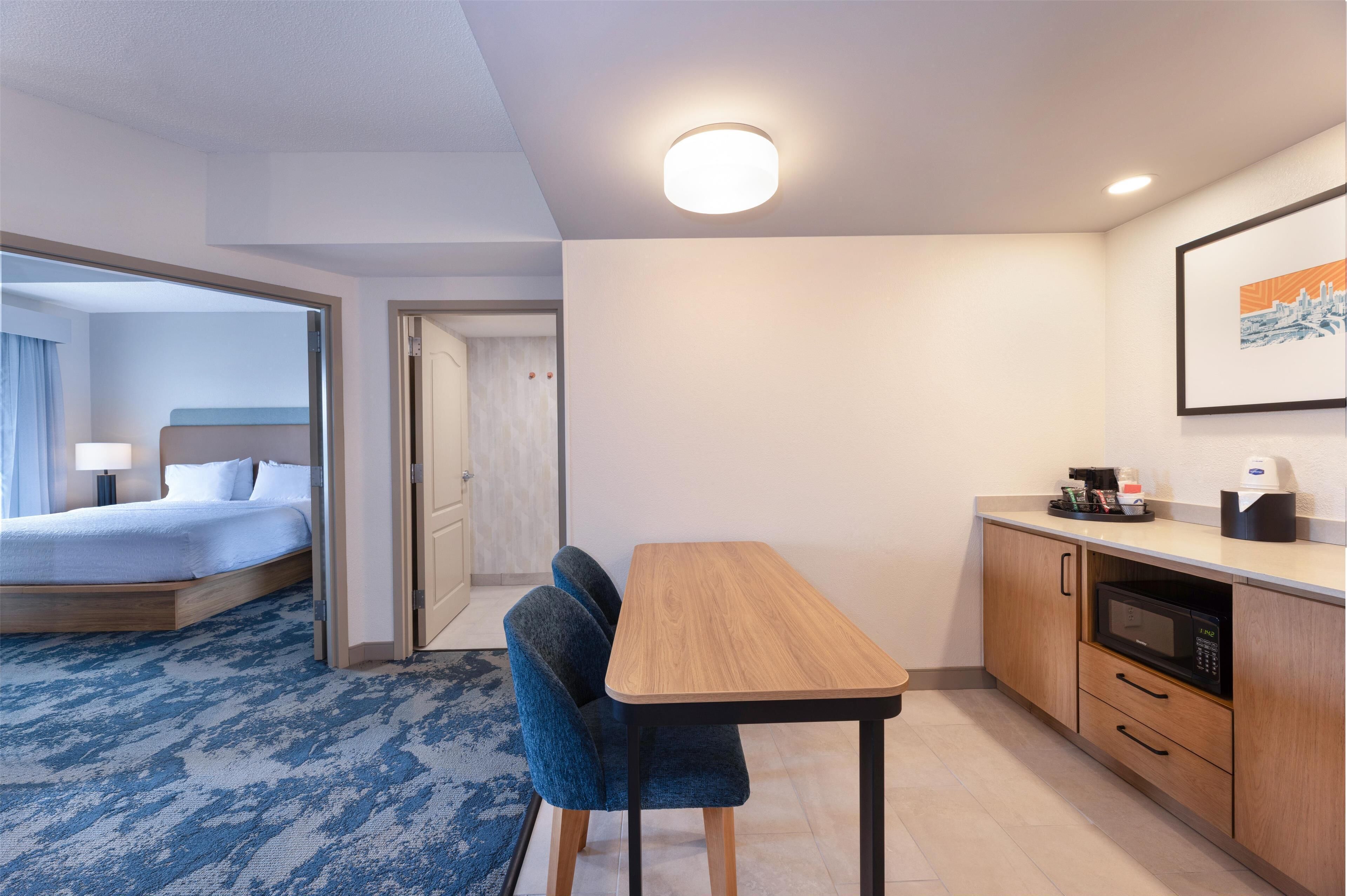 Een hotelkamer met een bed, een eettafel met stoelen, een magnetron en een kleine kitchenette.
