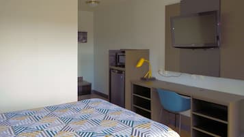 Een hotelkamer met een bed, een bureau met stoel, een televisie en een kleine koelkast.