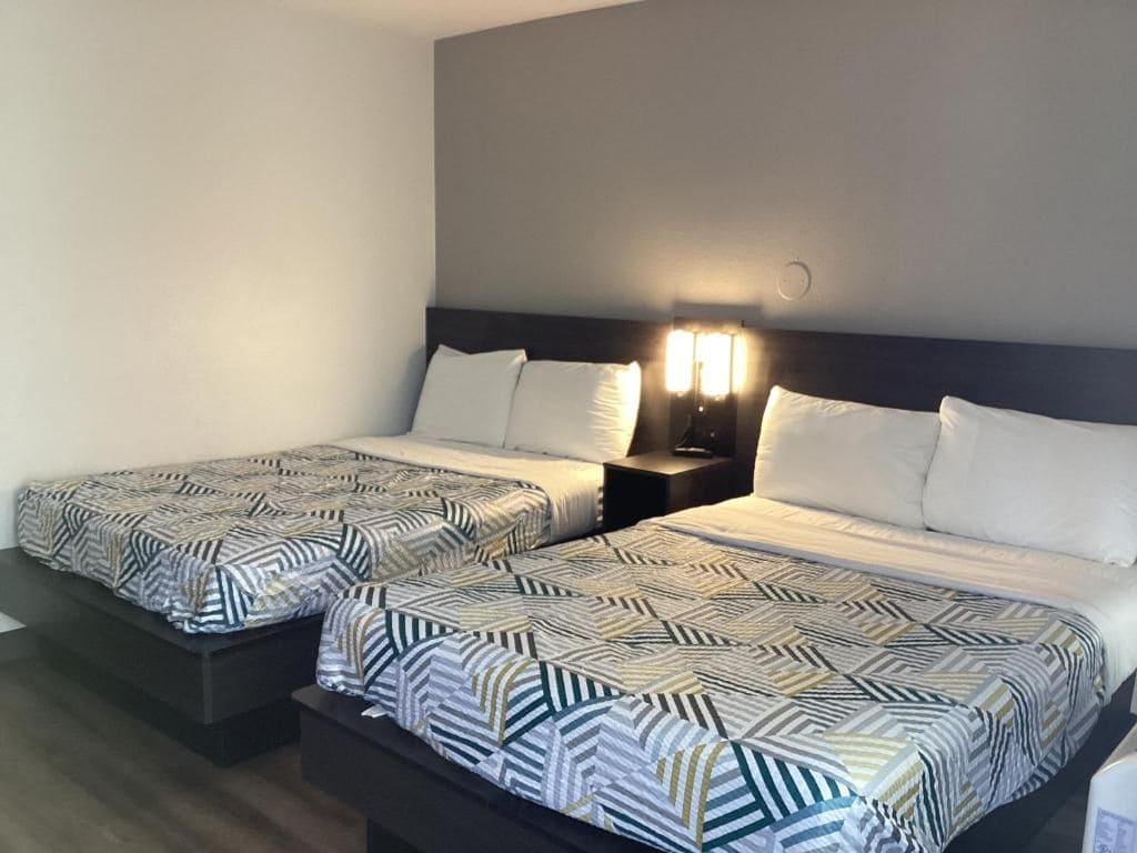 Ein Hotelzimmer mit zwei Betten, jeweils mit gemusterten Bettbezügen und einem Nachttisch mit Lampe.