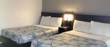 A hotel room with two beds, each with patterned bedding and a nightstand with a lamp.
